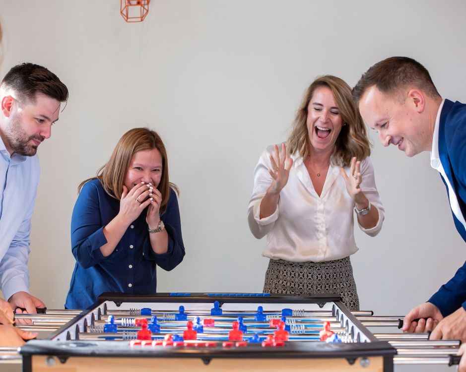 Colleagues playing a foosball game during a team-building activity, laughing and connecting.