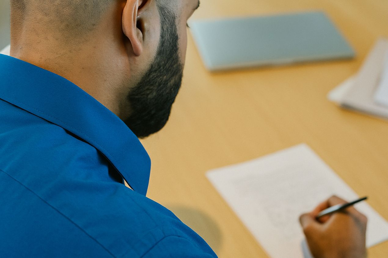 Employee in a blue shirt writing notes during a workplace training session, symbolising focus and professional development.