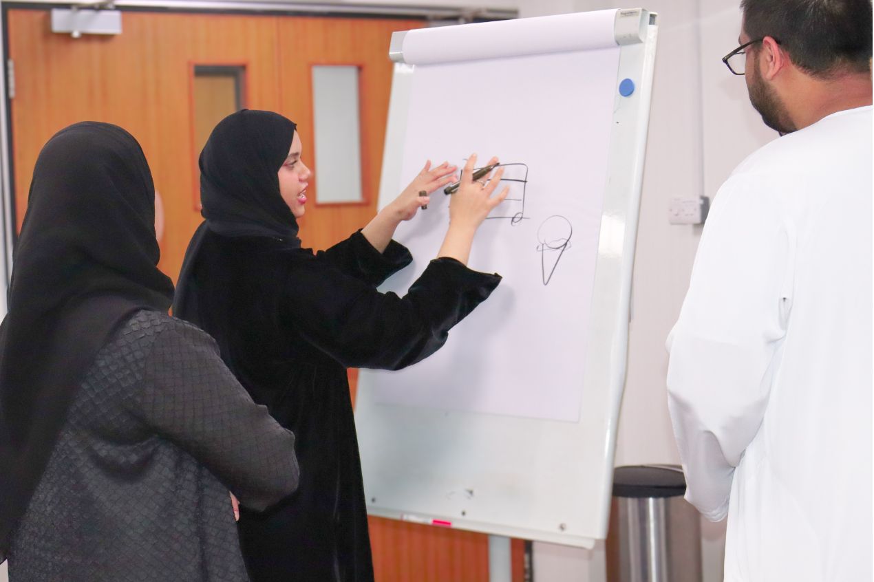 Female Emirati trainees presenting ideas on a flipchart in a LEAP leadership development session.