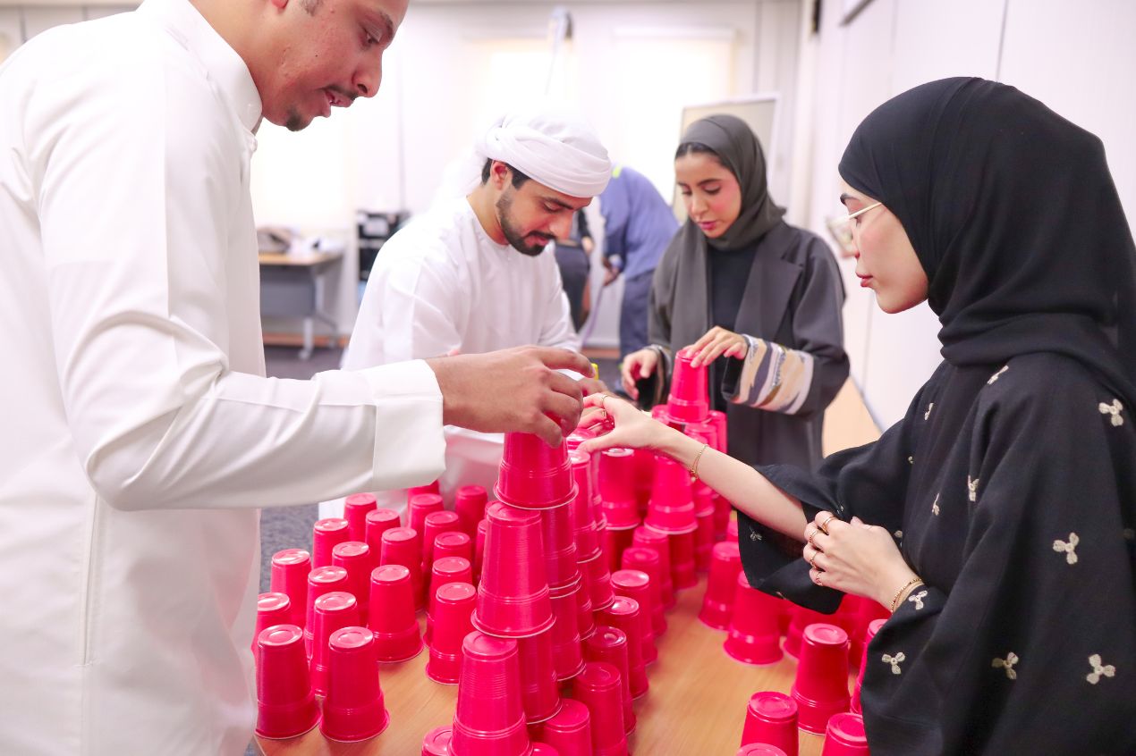 Graduate trainees working together to stack red cups in a teamwork and problem-solving activity.